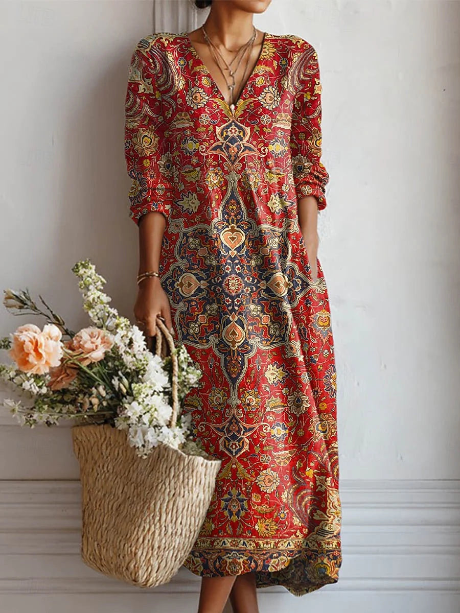 Woman wearing a floral maxi dress with intricate paisley print in crimson, gold, and navy tones, featuring a V-neckline and three-quarter sleeves