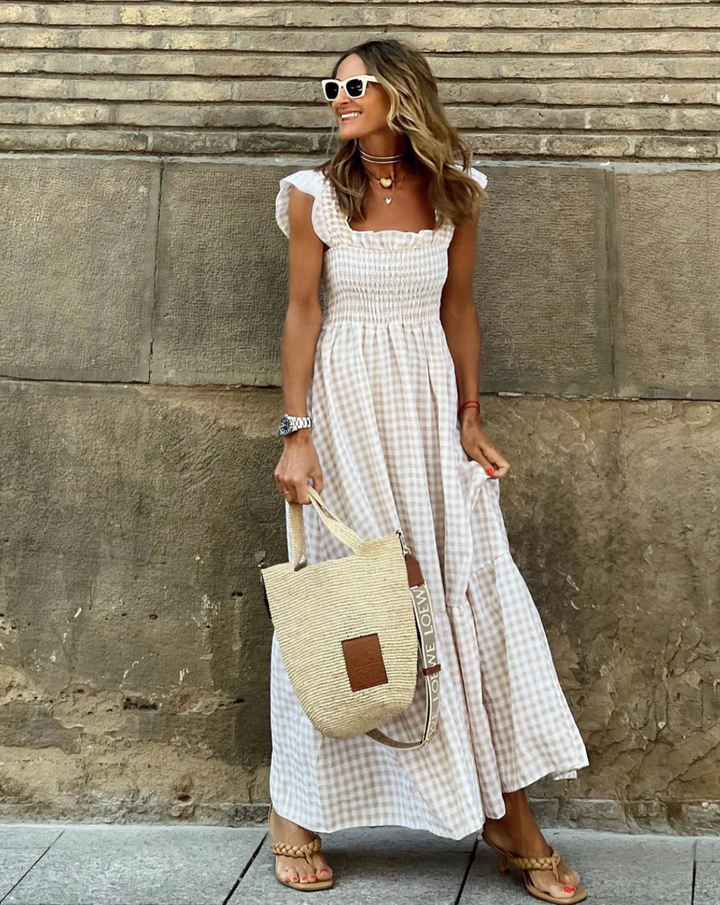 Woman wearing beige gingham smocked summer maxi dress with ruffled sleeves and tiered hem standing outdoors