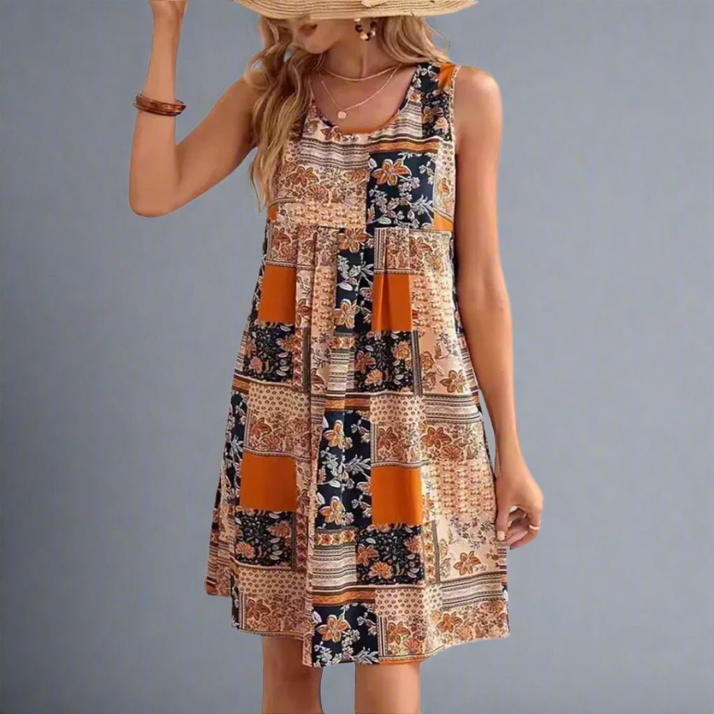 Front view of sleeveless mini dress featuring patchwork print with floral and geometric motifs in cream, amber, and navy