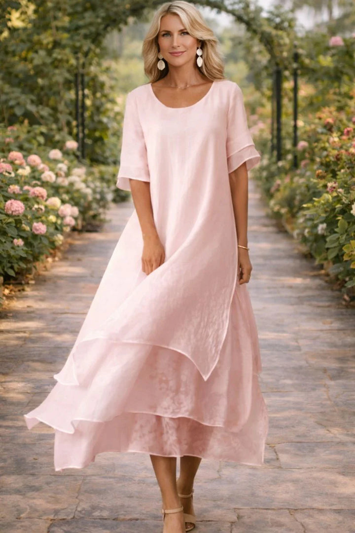 Woman wearing a pale pink layered midi dress with open neckline and flattering cut in a garden setting