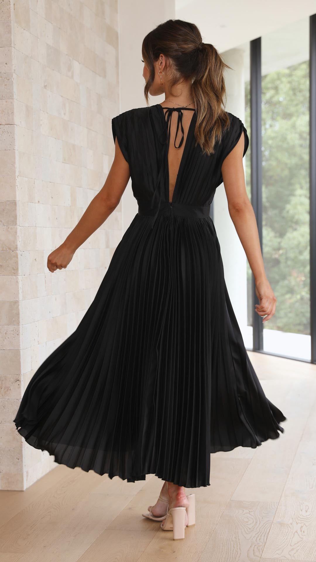 Side profile of women's V-neck pleated dress displaying midi length and flowing skirt