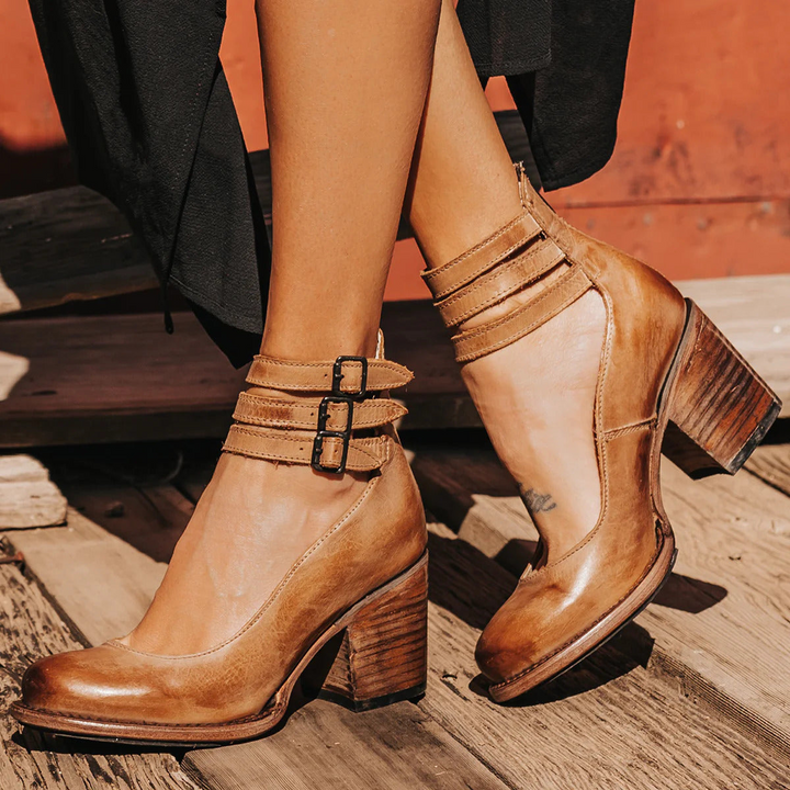 Woman wearing brown strappy ankle strap heels with double buckle detail and block heel on wooden deck